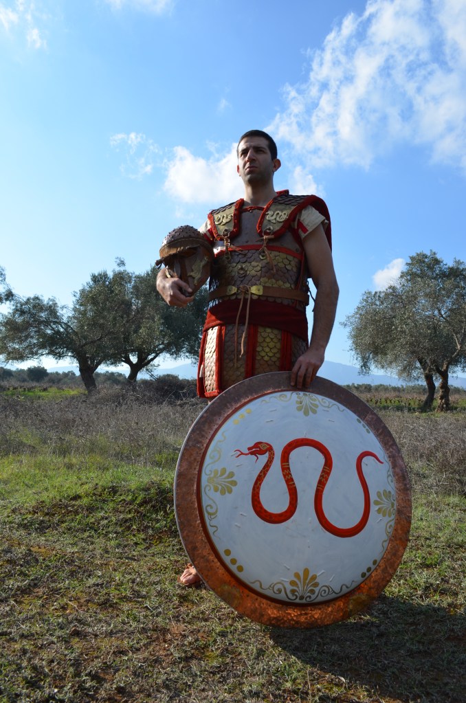 Αναπαράσταση Βαριά οπλισμένου Οπλίτη της Κλασσικής Περιόδου, ο οποίος φέρει ενισχυμένο με μπρούτζινες και χάλκινες φολίδες λινοθώρακα και ξύλινη ασπίδα τύπου "Οπλον". Σύλλογος Ιστορικών Μελετών ΚΟΡΥΒΑΝΤΕΣ